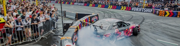 Drift car with smoking tyres in the Red Bull Drift Shifters competition and a large crowd watching