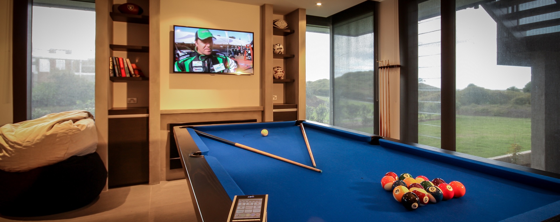 Man-cave with pool table, large TV, bean bags, books and memorabilia featuring home automation touchscreen control