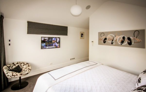 Bedroom with ceiling speakers and a wall mounted TV in front of bed