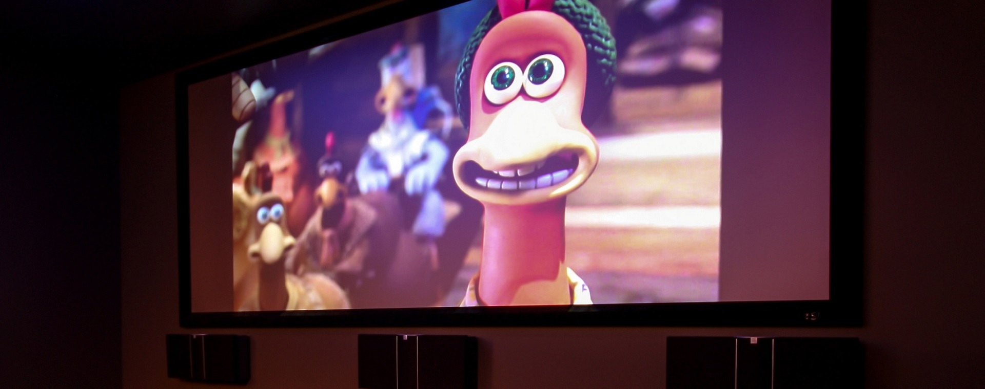 Large projector screen showing Chicken Run, with on-wall speakers beneath for a cinematic experience, controlled via a home auotmation system