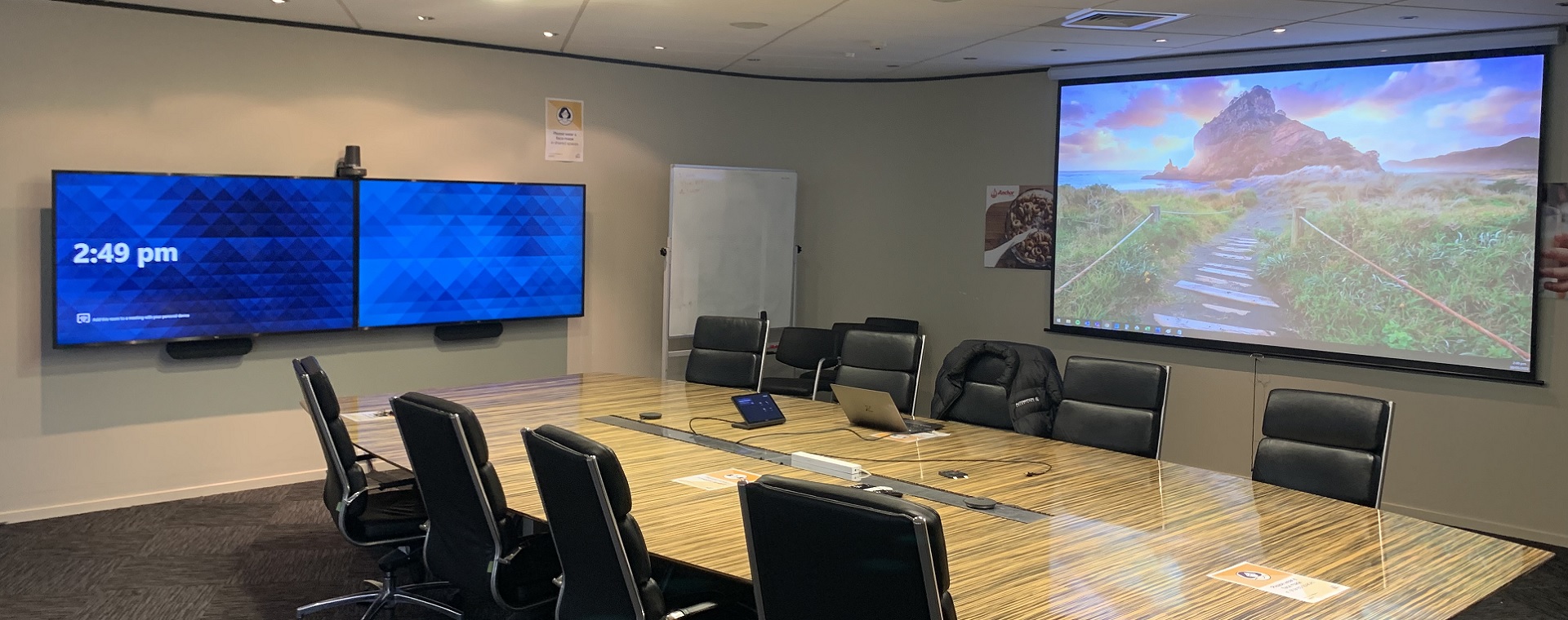 Medium sized meeting room at Fonterra with drop down projector screen and 2 large format display panels, control touchpanel on table and connections for 'bring your own device'