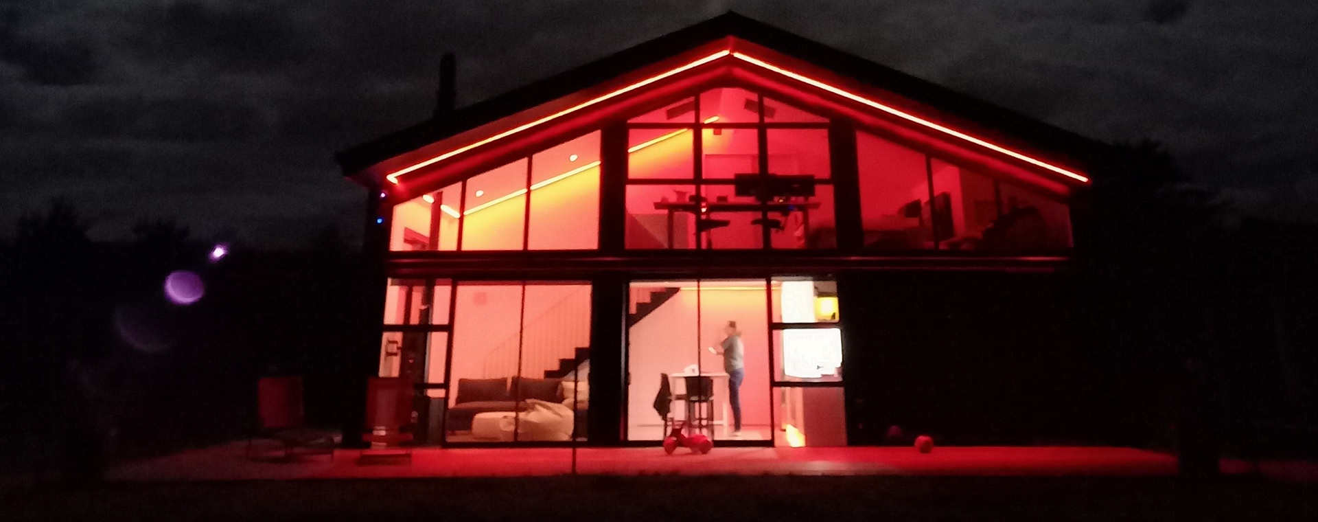 Off-grid home at night, with changeable colour LED light strips showing red lighting scene.